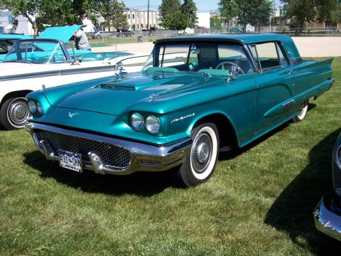 1972 Ford Ranchero - A classic teal Ford Thunderbird is displayed on a grassy field, with another vehicle partially visible to its left.