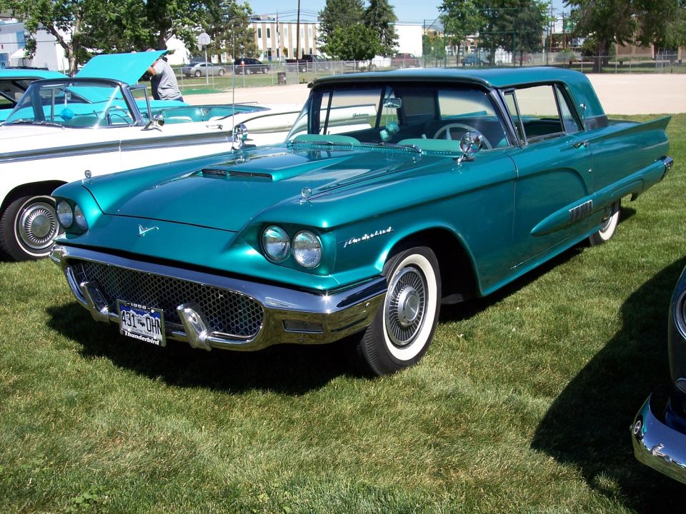 Teal 1958 Ford Thunderbird coupe parked on grass, another car to the left