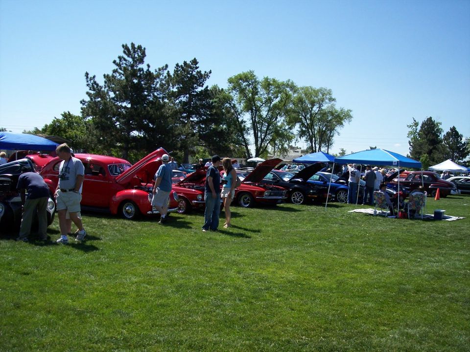Outdoor car show with several cars on display, some with hoods open. People are gathered around the vehicles