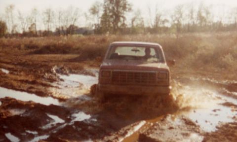 1981 Ford Bronco - Red SUV navigating a muddy terrain with water splashing.
