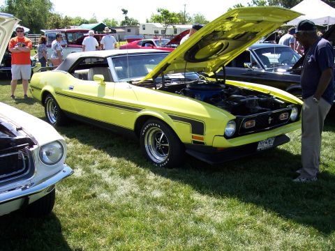 1972 Ford Ranchero - A yellow 1971 Ford Mustang convertible is displayed with its hood open at a car show, with other vehicles and people in the background.