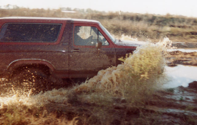 Red Ford Bronco driving through muddy water, splashing a lot
