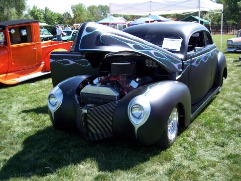 1972 Ford Ranchero - A matte black hot rod with custom flame paint and an exposed engine is displayed outdoors.