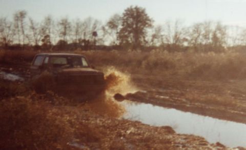 1981 Ford Bronco - A Ford Bronco navigates a muddy track, kicking up water.