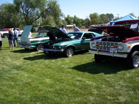 1972 Ford Ranchero - Three classic vehicles, including a 1969 Ford Mustang Mach 1 and a Ford Bronco, are displayed with their hoods open at an outdoor event.