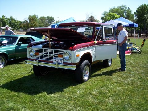 1972 Ford Ranchero - A two-tone red and white Ford Bronco is displayed with its hood open at an outdoor event, next to another vehicle.