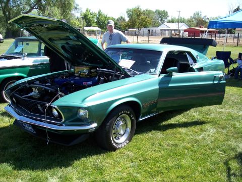 1972 Ford Ranchero - Green 1969 Ford Mustang Mach 1 at an outdoor car show with hood and door open.