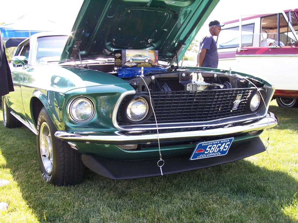 Green 1969 Ford Mustang with hood open, showing engine and a model car on display