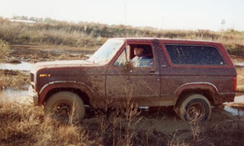 1981 Ford Bronco - Muddy 1981 Ford Bronco navigates a wet, grassy terrain.