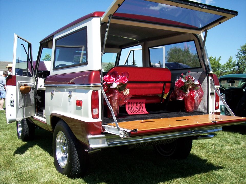 Two-tone red and white Ford Bronco with tailgate down, red seats, and floral arrangements