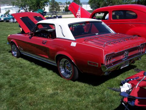 1972 Ford Ranchero - Red 1967 Ford Mustang with white vinyl roof and chrome luggage rack on back, parked on grass.