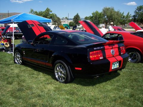 1972 Ford Ranchero - A black Shelby GT500 with red racing stripes is displayed at an outdoor car show with other vehicles.