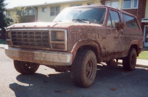1981 Ford Bronco - This heavily soiled SUV is shown from the front quarter angle, with its grille and body covered in mud.