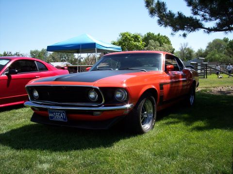 1972 Ford Ranchero - A classic orange Ford Mustang Boss 302 is displayed on a sunny day next to a red car.