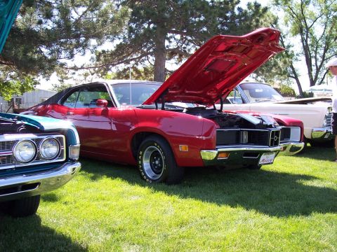 1972 Ford Ranchero - A red 1970s coupe with its hood open is parked on grass next to another vehicle.