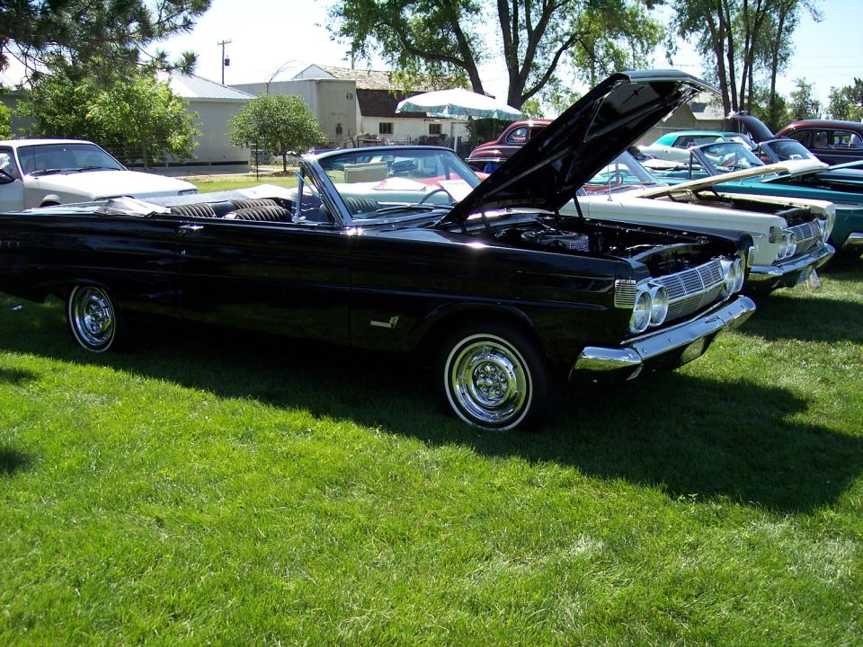 Black 1965 Mercury Comet convertible with hood open, parked in a line with other cars on grass