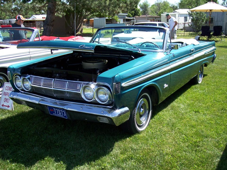Teal 1964 Mercury Comet convertible with hood open, parked on grass. Another car is partially visible to the left