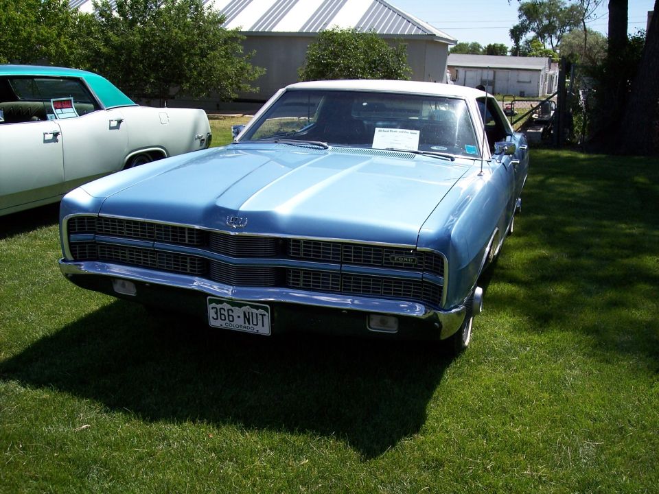 1968 Ford LTD front view, blue with white roof, parked on grass. Another car is partially visible to the left