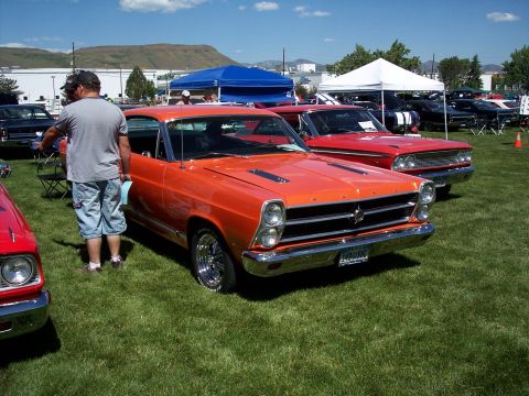 1972 Ford Ranchero - A classic orange Ford Fairlane GT is displayed at an outdoor car show with other vehicles and tents in the background.