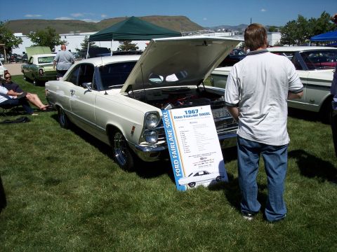 1972 Ford Ranchero - A 1967 Ford Fairlane 500XL is displayed with its hood open, alongside a descriptive sign at a car show.