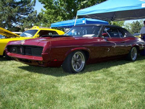 1972 Ford Ranchero - A maroon coupe with a black top and hood scoop is parked on grass next to a yellow vehicle.
