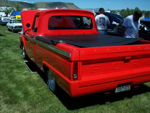 1972 Ford Ranchero - A bright red pickup truck is parked on a grassy field, with its hood up and a black tonneau cover over the bed.
