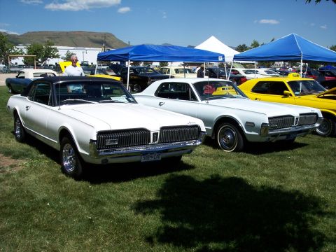 1972 Ford Ranchero - Two classic Mercury Cougars are displayed at an outdoor event with other vehicles and tents in the background.