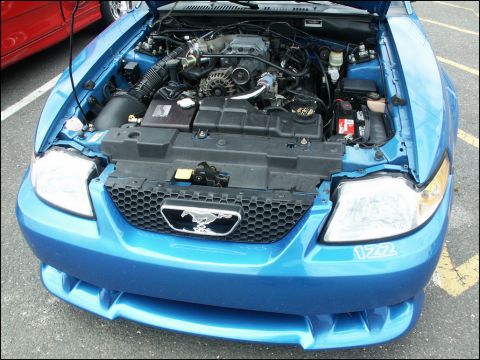2001 Mercury Grand Marquis - Front view of a blue Ford Mustang with its hood open, revealing the engine compartment. A red vehicle is partially visible on the left.