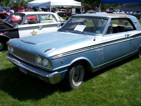1972 Ford Ranchero - A light blue coupe with a distinctive grille and side trim is parked on a grassy field, with other vehicles and tents in the background.