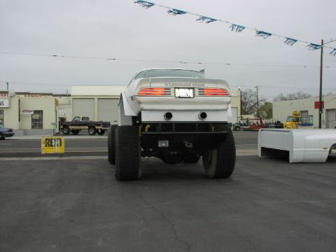 1981 Ford Bronco - Modified 1977 Pontiac Firebird with large tires is parked outdoors near buildings.