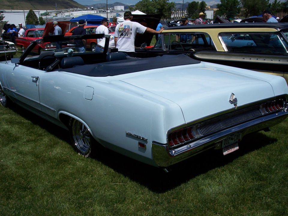 Light blue convertible with chrome wheels and a black top, seen from the rear
