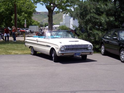 1972 Ford Ranchero - A white convertible with a blue interior is parked in front of a building. A black sedan is parked to its right.