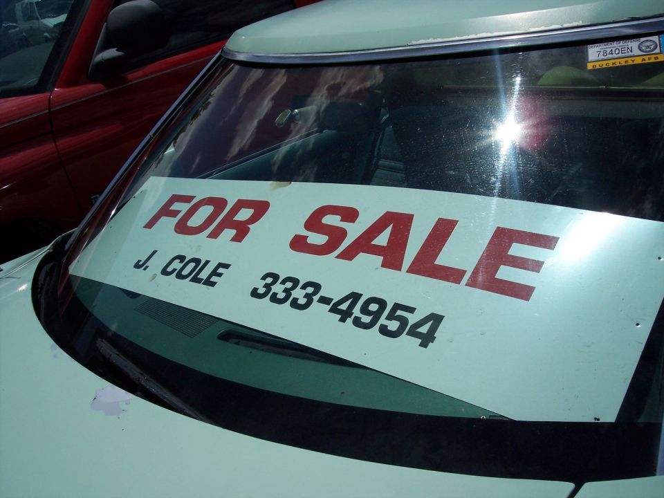 Light colored car's windshield with "FOR SALE" sign and phone number