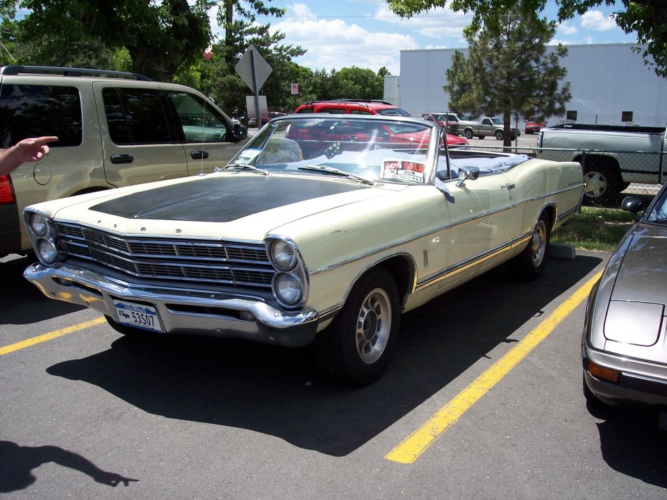 Pale yellow convertible with black hood parked in a lot. License plate reads 53507