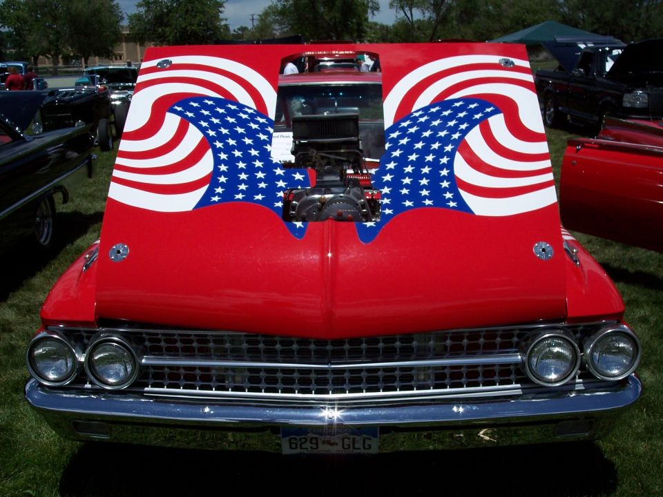 Red 1960s Ford with stars-and-stripes hood mural and exposed blower at a car show