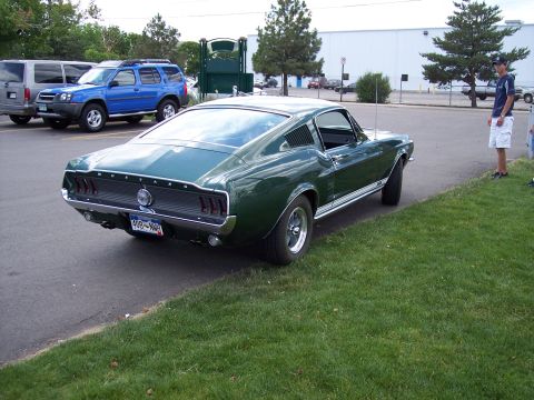 1972 Ford Ranchero - A green 1967 Ford Mustang is parked next to a grassy area, with other vehicles and a person in the background.