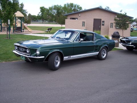 1972 Ford Ranchero - A pair of classic Ford Mustangs are parked at a park with a playground and restroom building in the background.