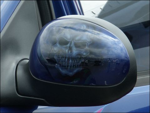 2001 Mercury Grand Marquis - Side mirror on a blue vehicle features an airbrushed skull graphic reflecting the sky and surroundings.