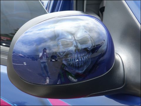 2001 Mercury Grand Marquis - A side mirror displays a skull airbrush design, reflecting a photographer and other vehicles.