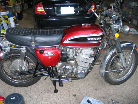 1994 Ford Bronco - A red 1975 Honda 750 Four motorcycle is parked indoors next to a black car.