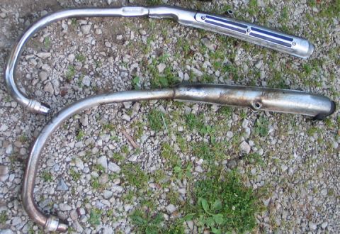 1994 Ford Bronco - Two motorcycle exhaust pipes, one chrome and one showing signs of use, lie on a gravelly surface.