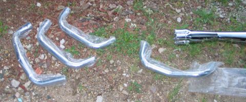 1994 Ford Bronco - Several chrome exhaust pipes are packaged and laid out on the ground next to some grass and dirt.