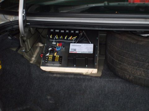 2004 Ford Crown Victoria - A car audio amplifier bolted to a carpeted plywood board mounted at an angle in a sedan trunk, with yellow, blue and red speaker leads land…