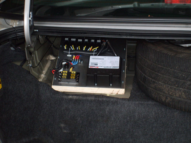 Trunk-mounted car audio amplifier on a plywood board with wiring and fuse block