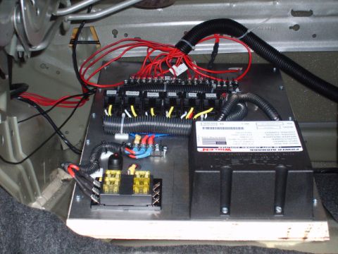 2004 Ford Crown Victoria - Emergency-equipment electrical panel mounted on a plywood board in a car's trunk, with a bank of automotive relays, a fused distribution bl…