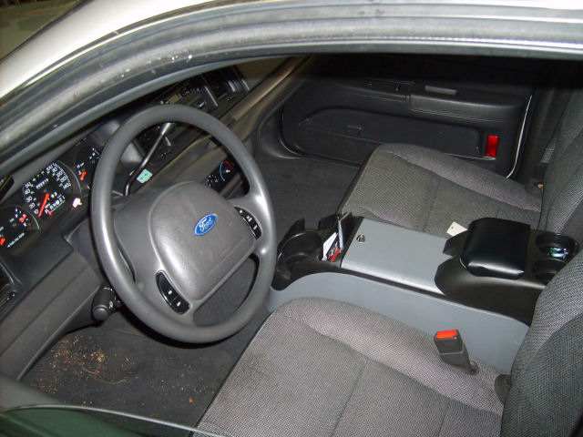 Interior view of a 2004 Ford Crown Victoria showing the steering wheel, dashboard, and front seats. A center console is visible between the seats