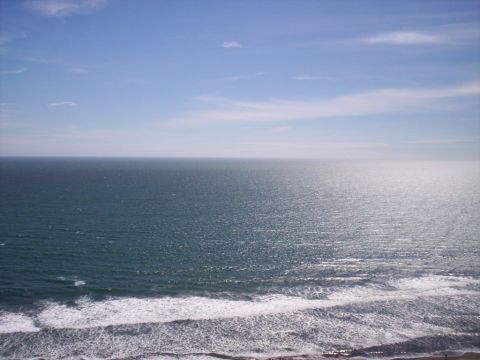 1989 Ford Bronco - Wide ocean view from a bluff, with sunlight glinting off the water and white surf breaking along the shoreline in the foreground under a ha…