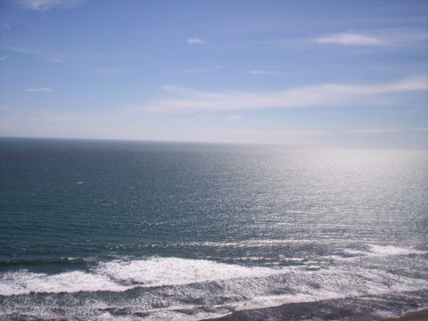 1989 Ford Bronco - The sun reflects off the deep blue ocean as waves roll towards a dark, rocky beach.