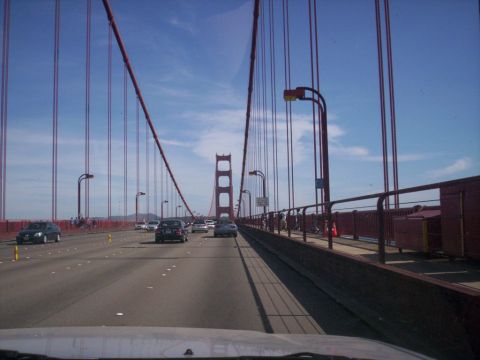 1989 Ford Bronco - Driving across the Golden Gate Bridge, with traffic visible on the roadway and pedestrians on the walkway.