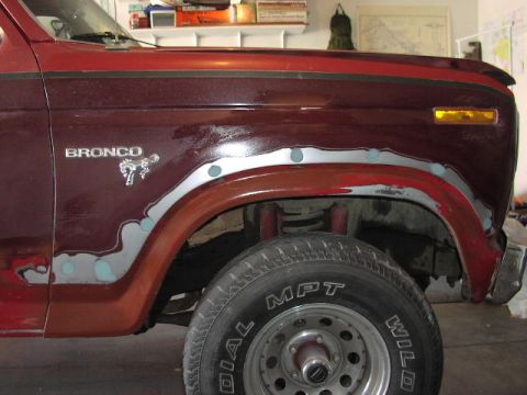 1981 Ford Bronco - The fender of a maroon Ford Bronco is shown with body filler and primer, indicating repair work.